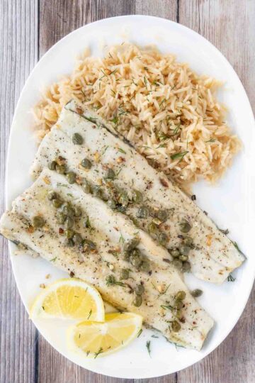 Pan fried rainbow trout with a lemon caper sauce and rice on a white plate.