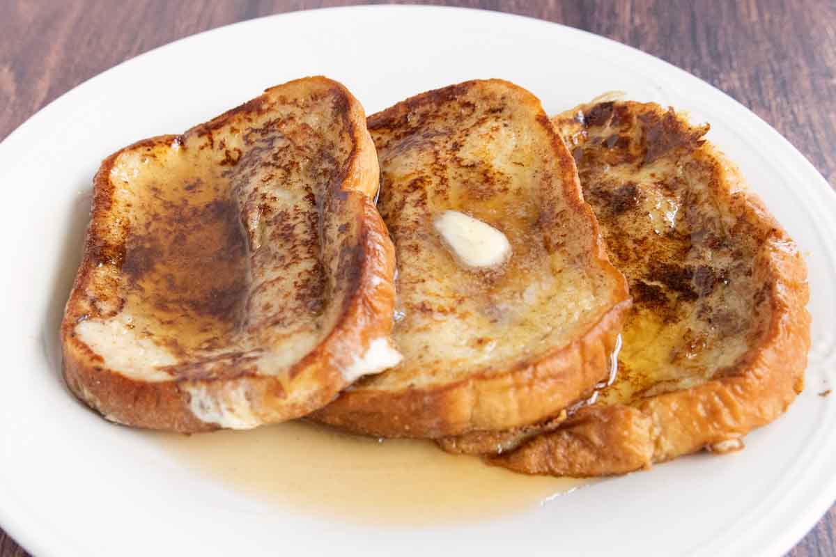 French Toast with butter, maple syrup and confectioners sugar on a white plate.