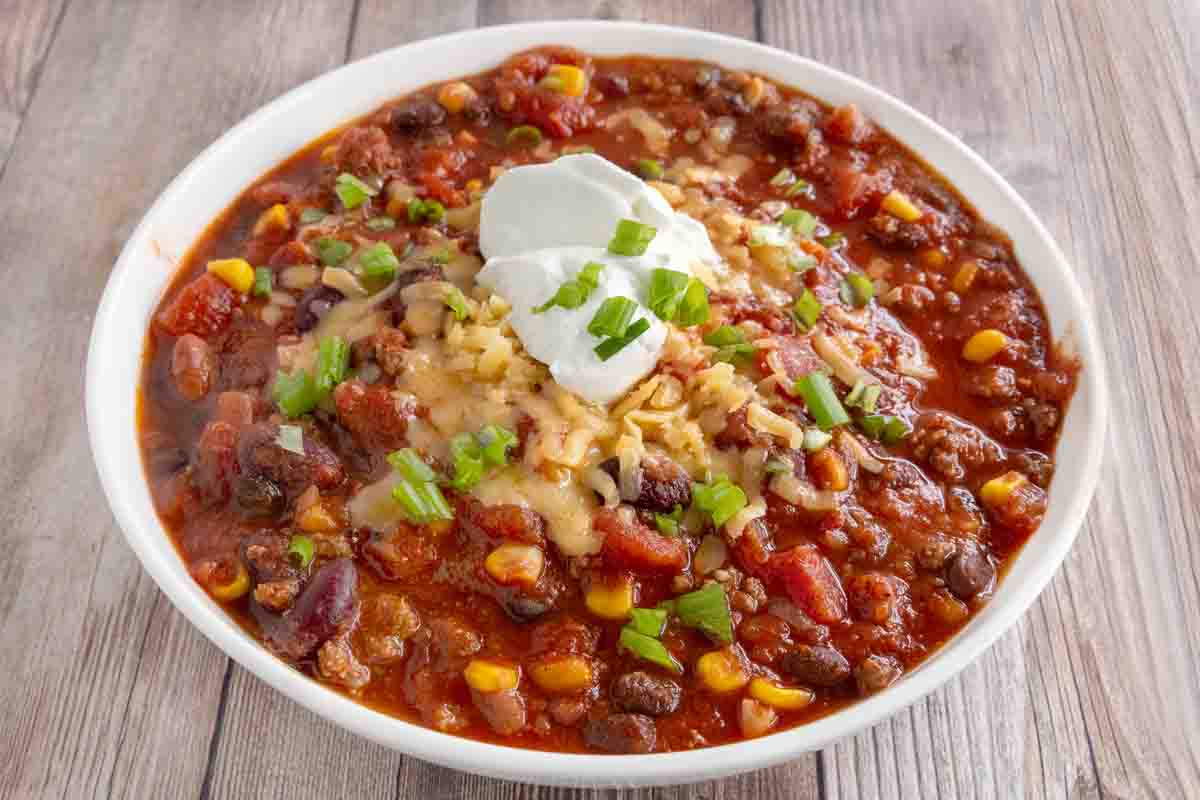 Slow cooker chili with shredded cheese and sour cream in a white bowl