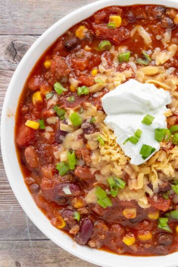 Slow cooker chili with shredded cheese and sour cream in a white bowl