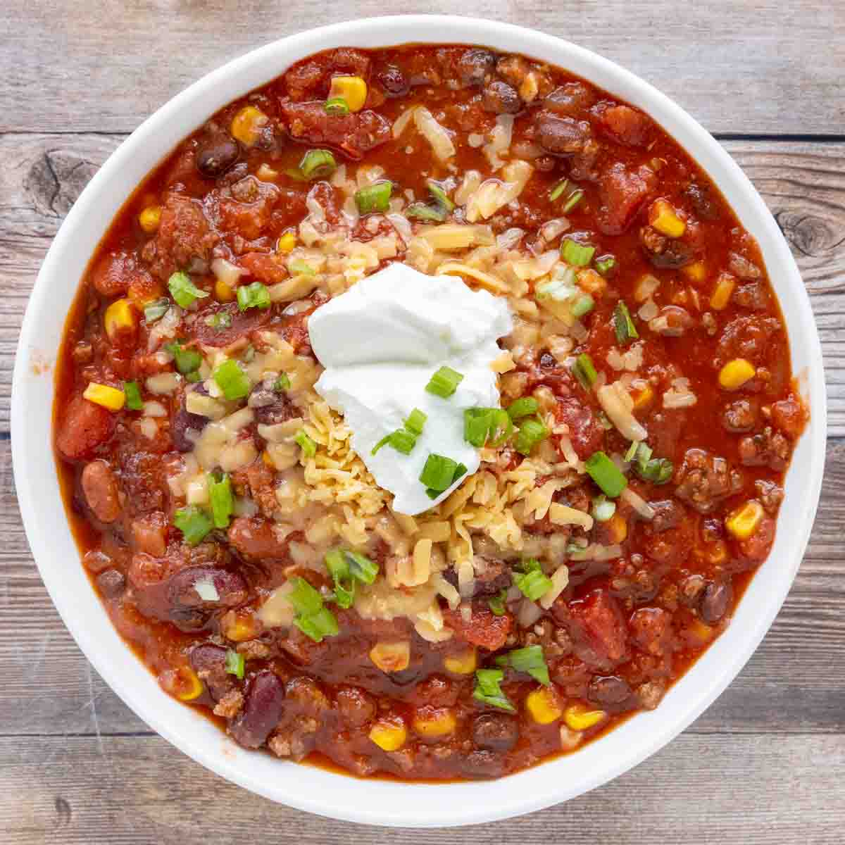 Slow cooker chili with shredded cheese and sour cream in a white bowl