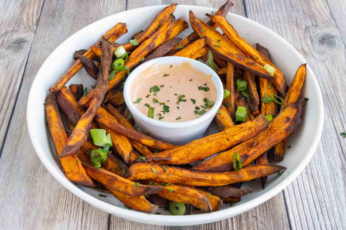 Air fryer sweet potato fries with sriracha mayo in a white bowl.