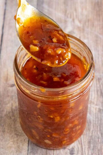 Honey sriracha sauce in a glass jar with a spoon coming out.