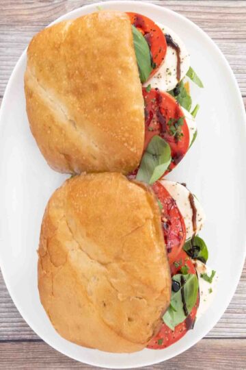 Two Caprese sandwiches on a white platter.