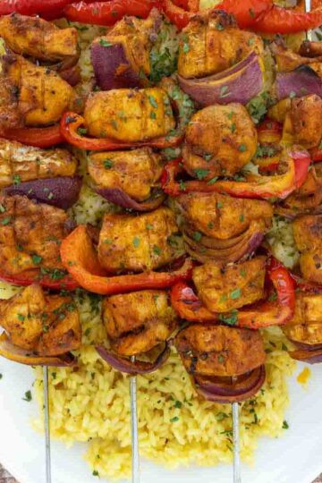 Pkate of chicken kabobs over yellow rice.