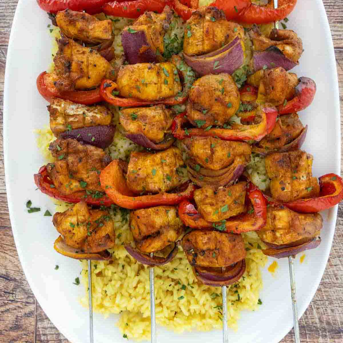 Pkate of chicken kabobs over yellow rice.