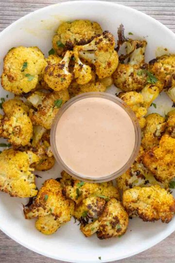 Bowl of oven-roasted cauliflower with spicy mayonnaise on the side.