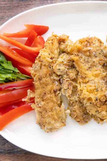 Picture of chicken tenders on a plate with parsley and red peppers.