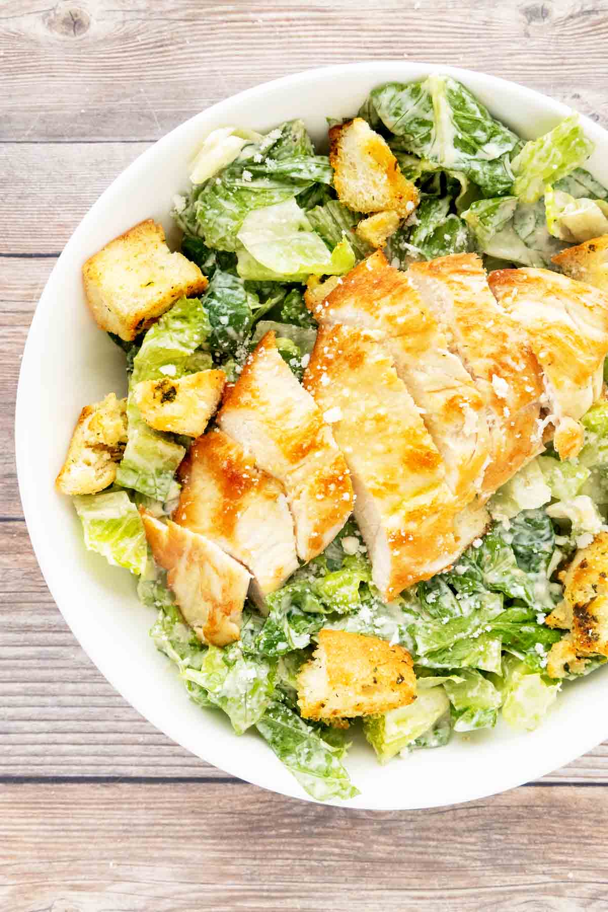 Bowl of Caesar salad with croutons topped with grilled chicken.