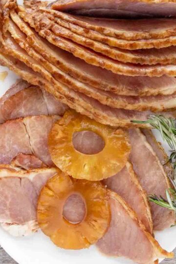 Plate with a slow-cooker ham, rosemary, and pineapple slices.