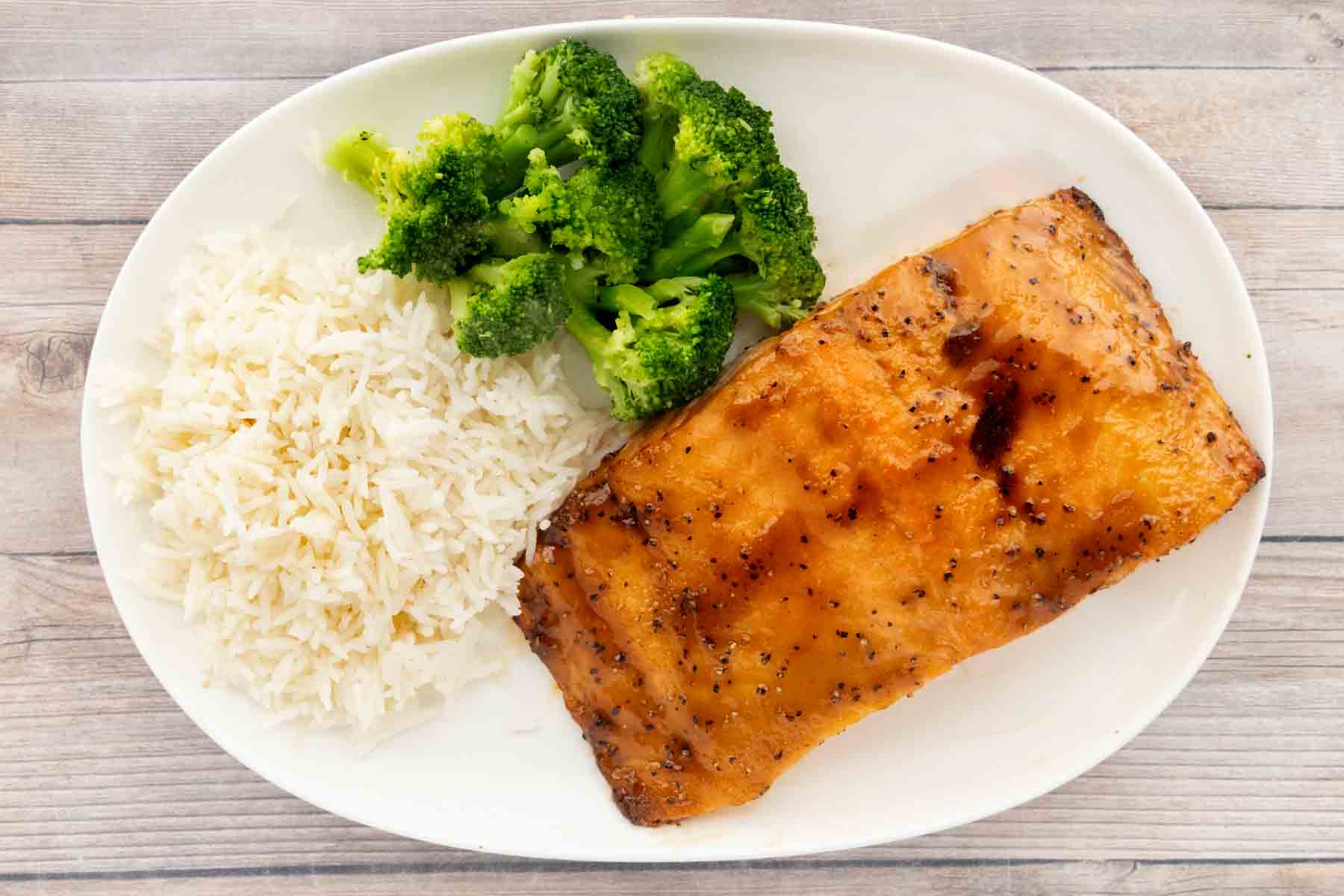 Teriyaki salmon on a plate with white rice and broccoli, garnished with sesame seeds. 