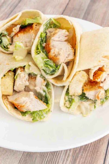 A plate with two chicken Caesar wraps on it, both sliced in half.