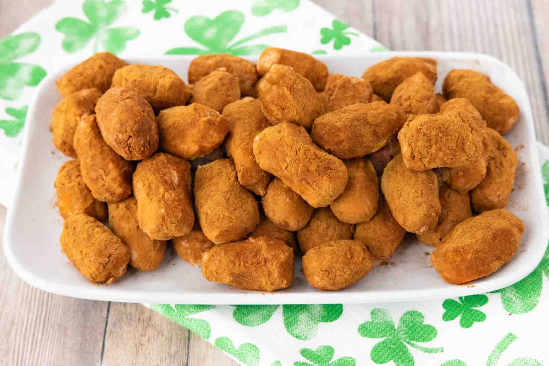 A plate of irish potatoes candies stacked high. Sitting on top of a white towel with green clovers on it. 