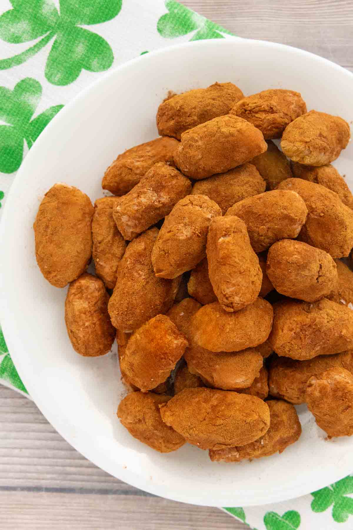 A plate of irish potatoes candies stacked high. Sitting on top of a white towel with green clovers on it. 