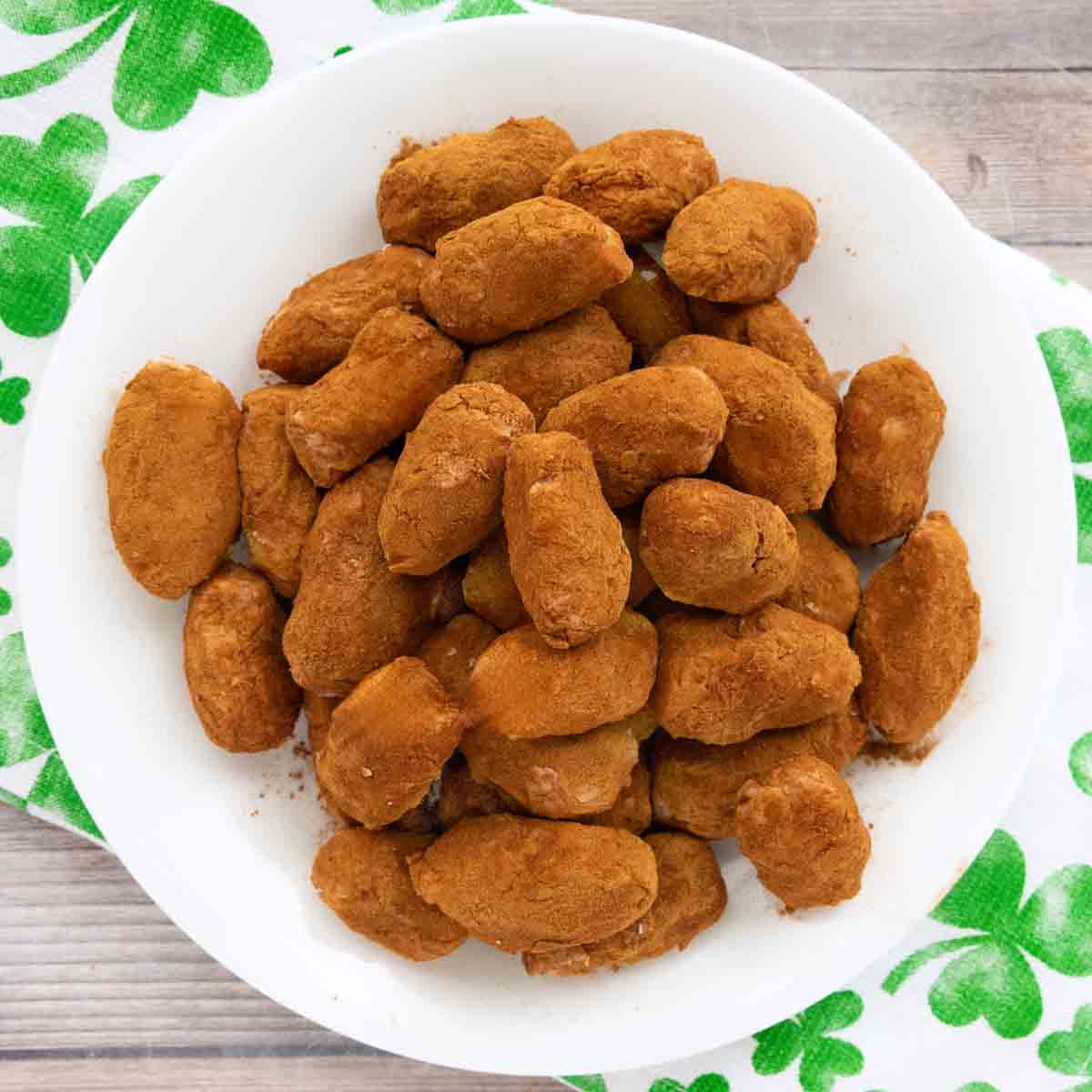 A white plate of Irish Potatoes Candy is stacked in a pile. Sitting on top of a white towel with four-leaf clovers imprinted on it.